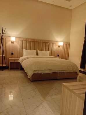 A bedroom with a large bed, wooden headboard, bedside lamps, and a wooden nightstand. - Luluat Althuraya Serviced Apartments (Riyadh)