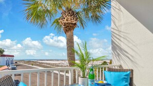 A balcony with a table set for two, a bottle of Pellegrino water, and a view of the beach and ocean.