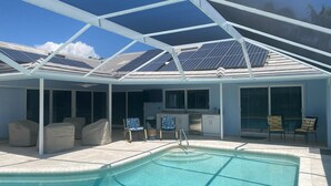 Ein überdachter Außenpool mit Terrassenbereich, Solaranlage auf dem Dach und Küchenzeile mit Fernseher.