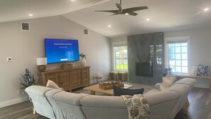 Ein modernes Wohnzimmer mit einer großen Eckcouch, einem flachbildfernseher an der Wand, einem Deckenventilator und einem Kamin.