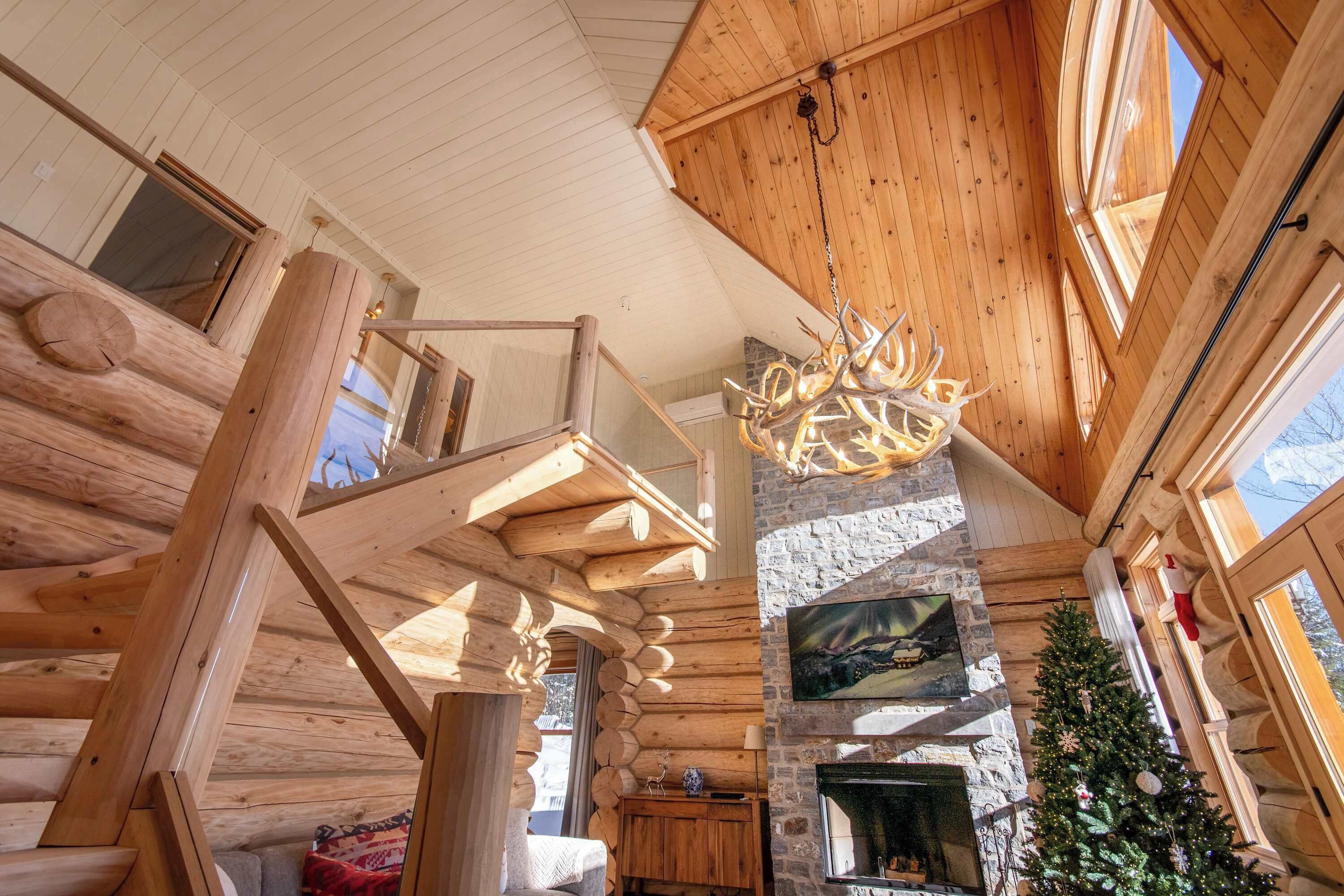 Ein Blockhaus-Interieur mit Kamin aus Stein, einer Holztreppe und einem Weihnachtsbaum.