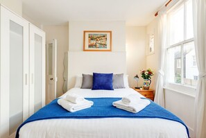 A hotel room with a bed, a painting on the wall, and a window with curtains. - Charming 2-bedroom House in Vibrant Fulham, London (London)