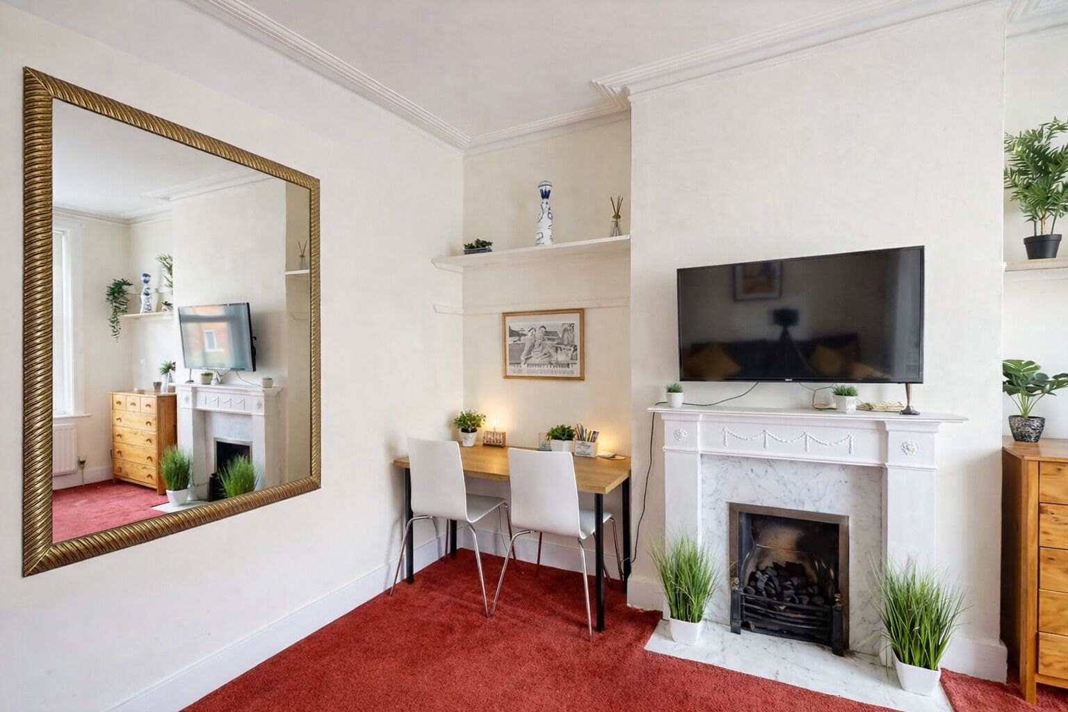 A living room with a fireplace, a television, a dining area with chairs, a large mirror, and a red carpet.