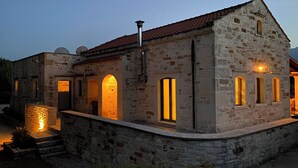 A stone building with arched doorways and windows, illuminated by warm lighting. - Traditional stone house for rent in Crete in a quiet location (Vamos)