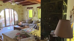 A room with a stone fireplace, a wooden ceiling, and a bed with a view through a large arched window. - Traditional stone house for rent in Crete in a quiet location (Vamos)