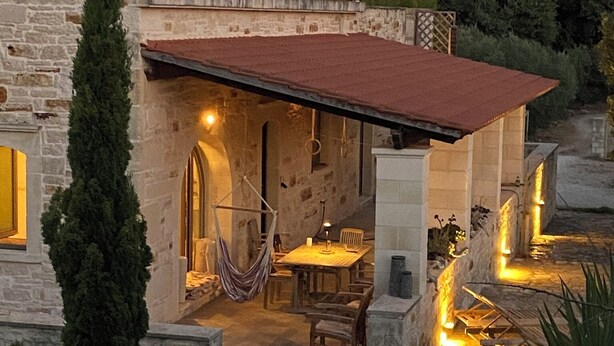 A stone house with a red-tiled roof, a hammock, and a table with chairs outside. - Traditional stone house for rent in Crete in a quiet location (Vamos)