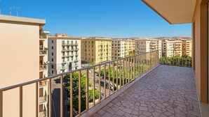 A balcony with a tiled floor and metal railing, overlooking a row of multi-story residential buildings.