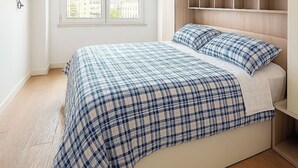 Une chambre à coucher comprenant un lit, une fenêtre avec des stores, un téléviseur fixé au mur et des placards intégrés.