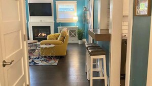 Un salon avec une cheminée, un canapé jaune, une table basse blanche et un tapis à motifs.