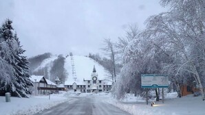 Une route enneigée menant à un bâtiment doté d’un clocher, entouré d’arbres chargés de neige et d’un panneau indicateur.