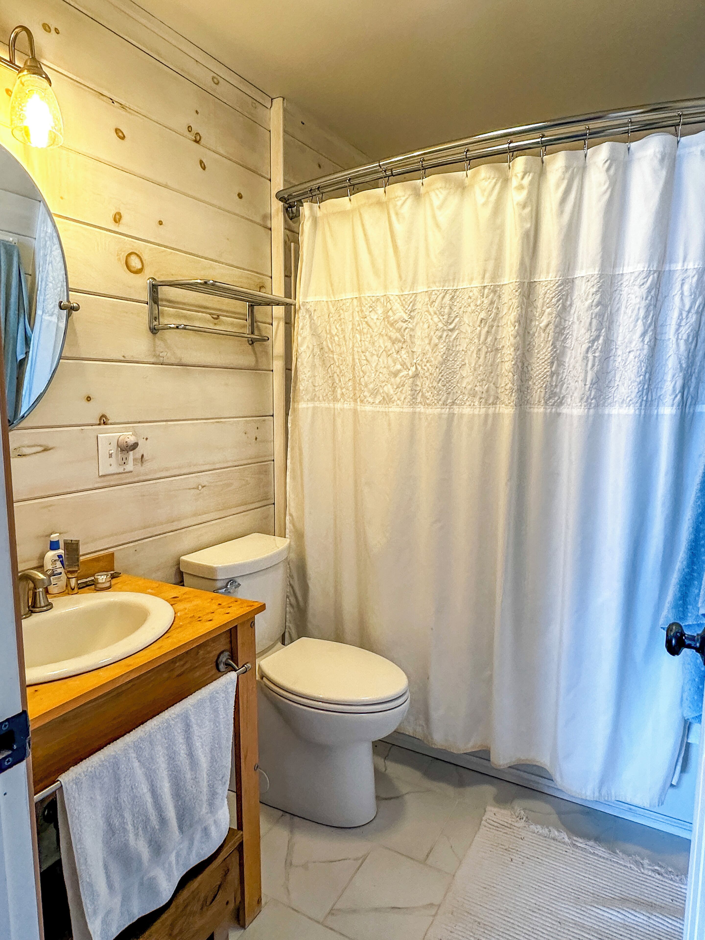 A bathroom with a wooden wall, a white toilet, a sink with a mirror, and a shower curtain.