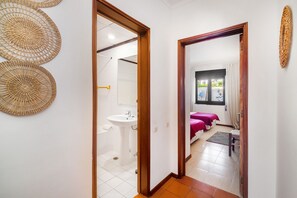 Enter a serene bedroom area with a comfortable bed, pedestal sink, and wicker decor.