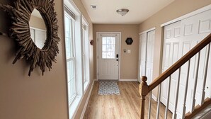 Un couloir doté d’un plancher en bois, d’un escalier en bois, d’une porte blanche au fond et d’un miroir décoratif accroché au mur.