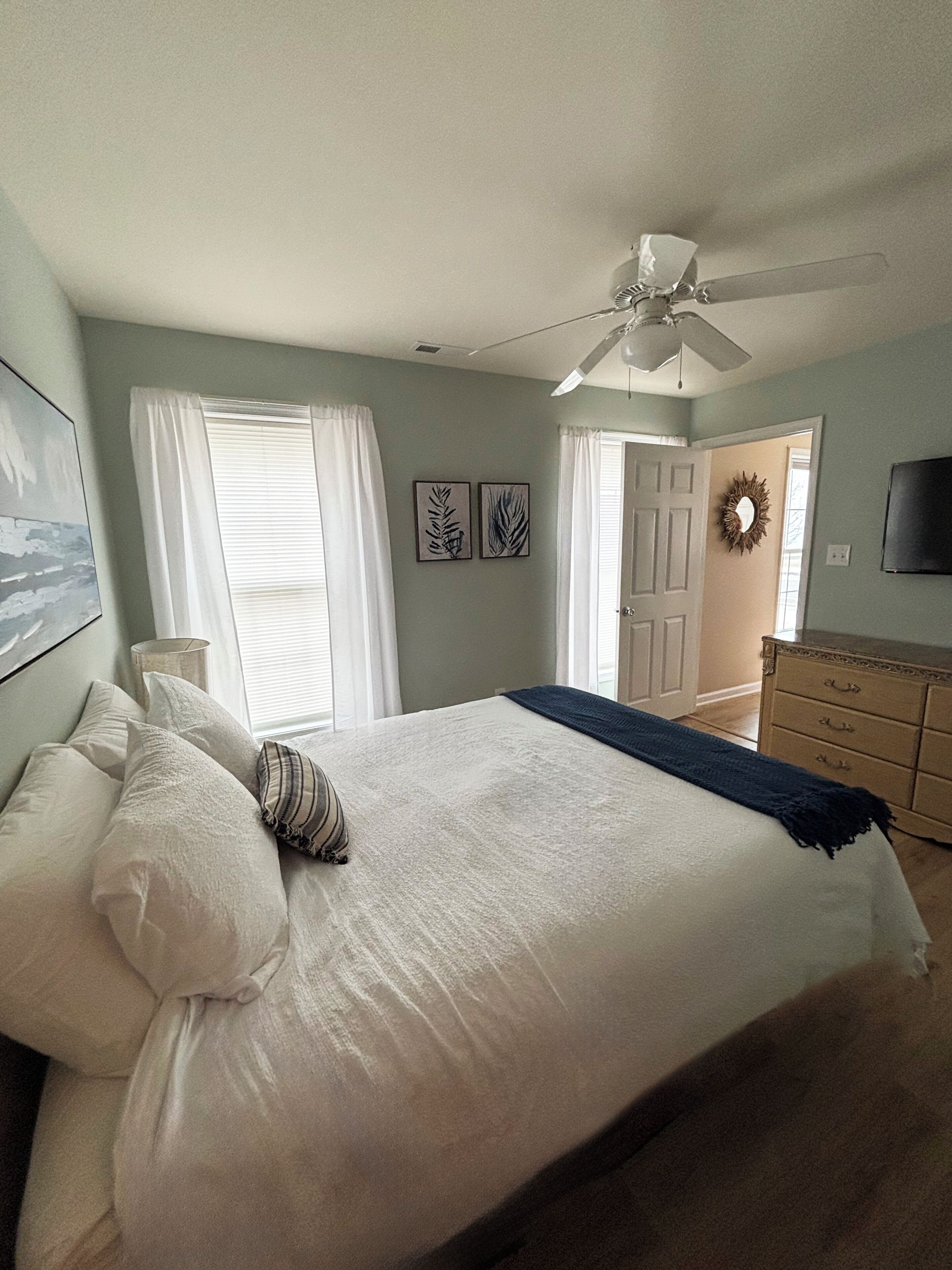 Ein Schlafzimmer mit einem großen Bett, einem Deckenventilator, einer Kommode und einem an der Wand befestigten Fernseher.