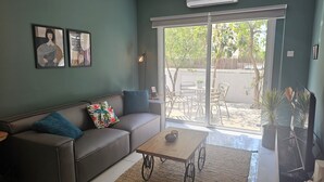A living room with a sofa, coffee table, and a sliding glass door leading to an outdoor patio area with chairs and potted plants.