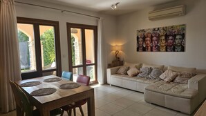 A living room with a dining table, a sofa, and a painting on the wall. - 62 APH - Stay Aphrodite Hills Apartment (Kouklia)
