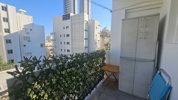 A balcony with a view of surrounding buildings, a small table, and a blue chair.