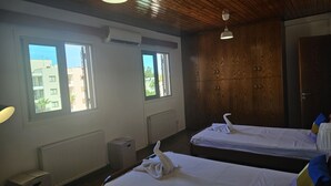 Habitación de hotel con dos camas, armario de madera y amplios ventanales con vistas a edificios.