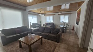 Amplia sala de estar con techo de madera, sofás grises, una mesa de centro de madera y un comedor con mesa de vidrio y sillas.