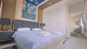 A bedroom with a large bed, two bedside tables with lamps, a wardrobe, and a painting on the wall. - 162 LCA - Stay Van Gogh Apartment (Larnaca)