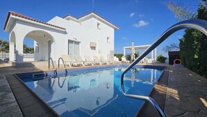 En swimmingpool med solstolar och en vit byggnad med valv i bakgrunden.