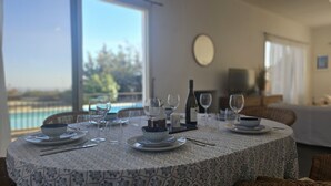 Ein Esstisch, gedeckt für eine Mahlzeit, mit Blick auf einen Swimmingpool und viel Grün.