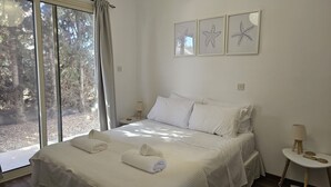 Ein Schlafzimmer mit einem Bett, zwei Nachttischen, einem Fenster mit Vorhängen und drei gerahmten Bildern von Seesternen an der Wand.
