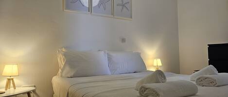 A neatly made bed with white linens, two bedside lamps, and three framed starfish art pieces on the wall.