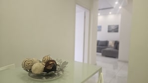 Un intérieur moderne au design minimaliste, comprenant une table en verre agrémentée d’objets décoratifs, un canapé blanc et un couloir épuré et lumineux.