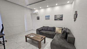 Un salon moderne avec un canapé gris, une table basse en bois et un petit téléviseur.