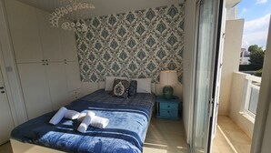 A bedroom with a bed, a nightstand, a lamp, and a patterned wallpaper. - 27 NIC - Stay Alex s House (Strovolos)