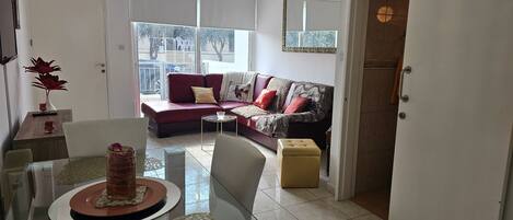 A modern living room with a red sofa, a glass dining table, and a view of the outdoors through large windows.