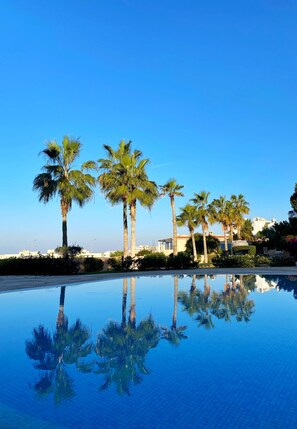 A pool with palm trees and a building in the background. - 67 KPF - Stay King s Palace (Paphos)