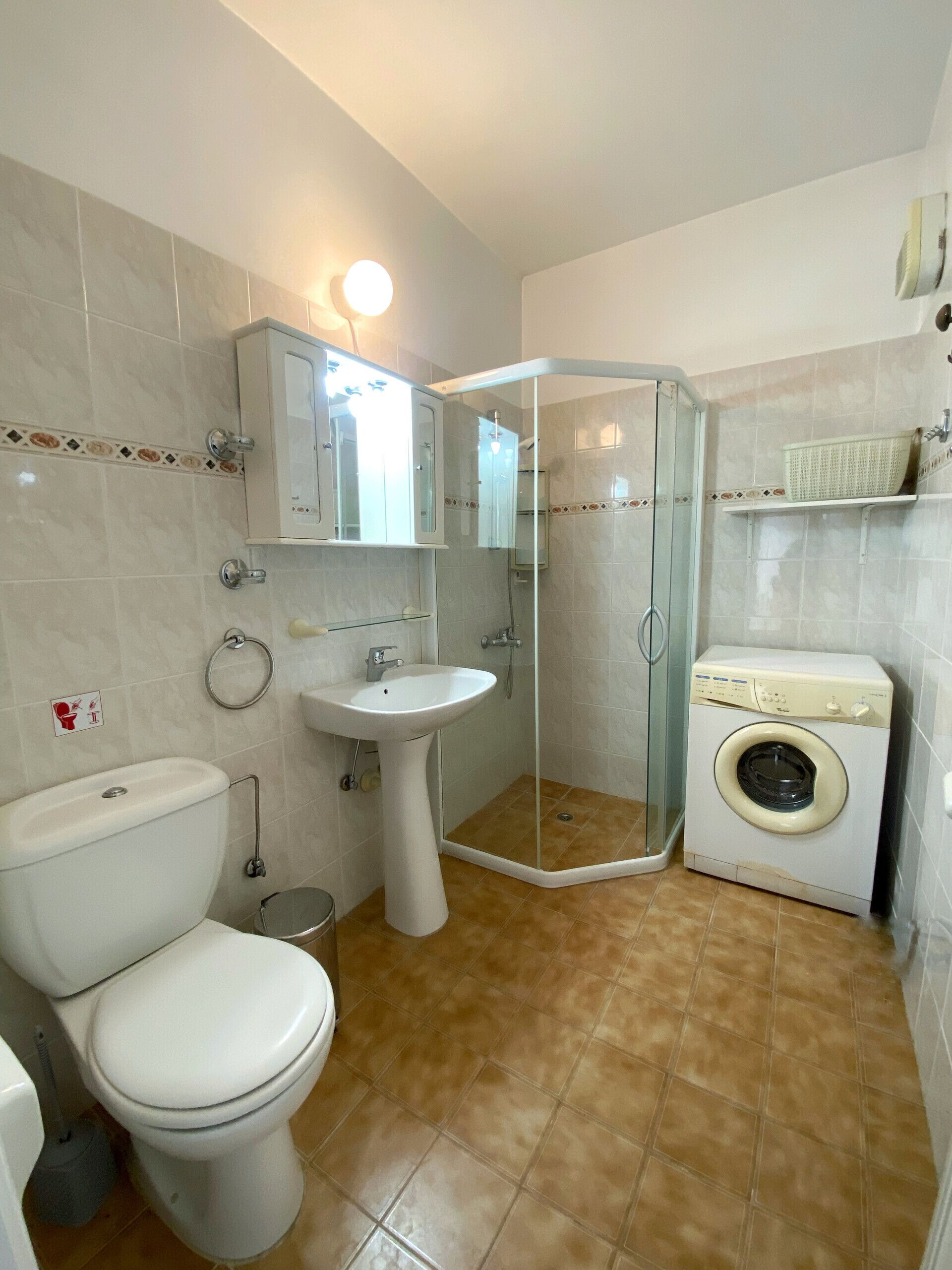 A bathroom with a toilet, sink, shower, and washing machine.