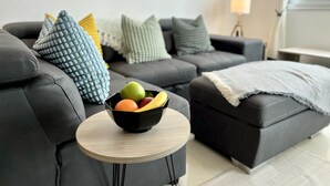 Un salon moderne avec un canapé d’angle gris, une table basse ronde en bois et un saladier rempli de fruits.
