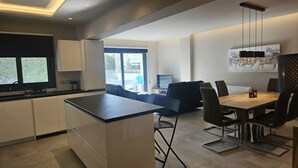 A modern kitchen with a large island, a dining area with a wooden table and chairs, and a living space with a sofa and a TV.