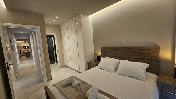 A modern bedroom with a large bed, wooden headboard, and a walk-in closet.