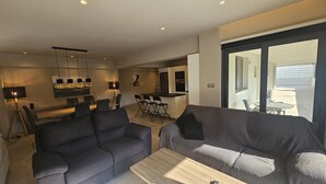 A modern living room with a sofa, a coffee table, and a dining area with chairs and a table.