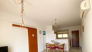A living room with a sofa, coffee table, and TV stand. There is a dining area with a table and chairs. The room has a kitchen in the background. - 43 MND - Stay Meadow Vista Apartment (Mandria)