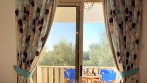 A room with a sofa, a table with a bowl of nuts, and a view of an outdoor patio with chairs and a table. - 43 MND - Stay Meadow Vista Apartment (Mandria)
