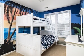 Une chambre avec des lits superposés, ornée d’une fresque représentant un coucher de soleil et des palmiers.
