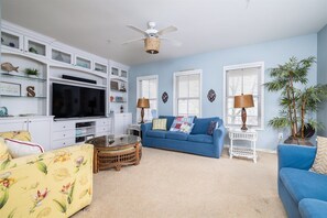 A living room with a television, blue sofa, white cabinets, and a ceiling fan.
