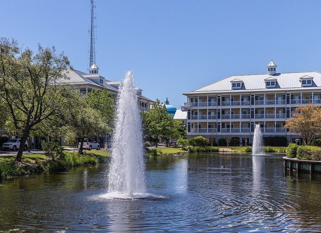A hotel with a fountain in the courtyard, surrounded by trees and a body of water.