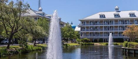 A hotel with a fountain in the courtyard, surrounded by trees and a body of water.