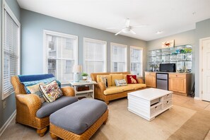 Un salon comprenant un canapé, deux fauteuils, une table basse et un coin cuisine avec des placards et un réfrigérateur.