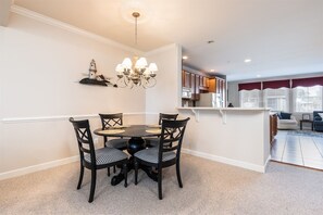 A dining area with a round table and chairs, a chandelier, and a kitchen in the background. - Sunset Island 3 Fountain Drive West (Ocean City)