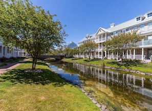 A residential area with a narrow waterway, white houses with balconies, and a tree-lined pathway.