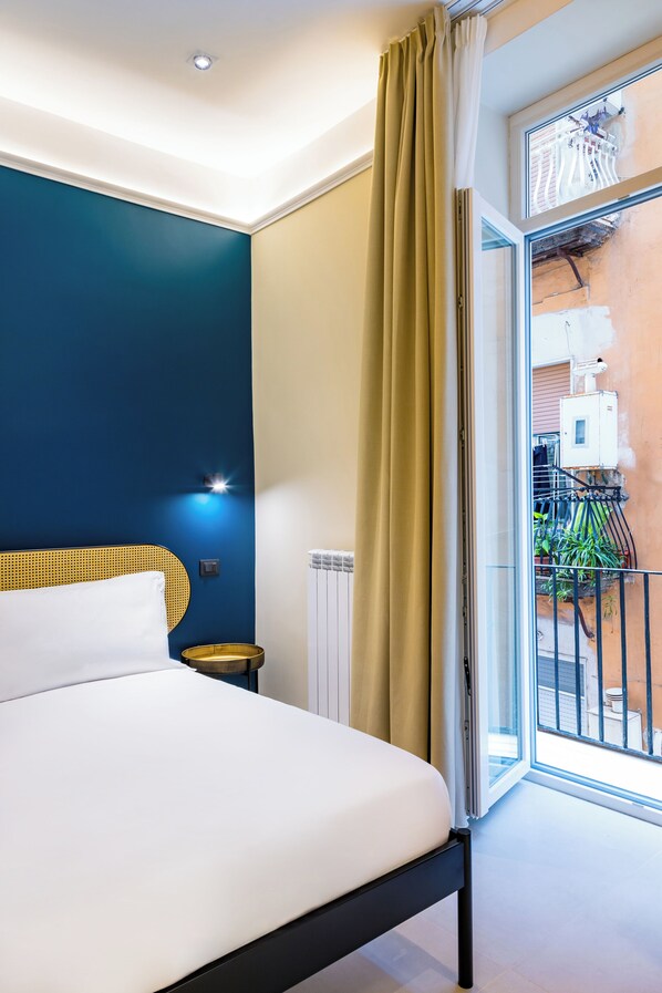 Relax in a spacious room with a large bed, a window offering a view of the outdoor area, and a balcony with potted plants.