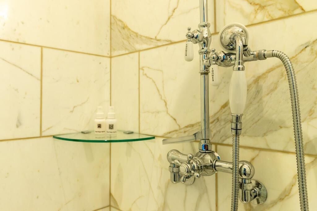 Un baño con ducha, repisa de vidrio y pared de mármol.