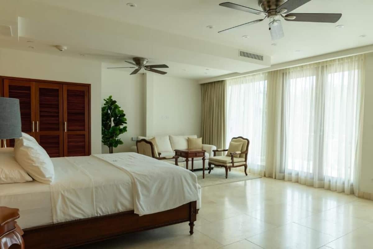 A spacious hotel room with a large bed, two chairs, a small table, and a ceiling fan.